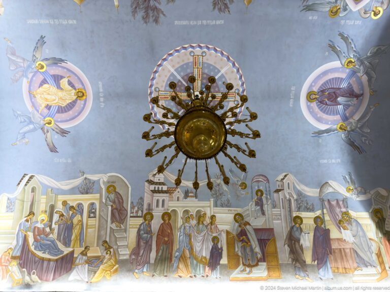 Painted cathedral ceiling with many biblical scenes arranged around a central metal fixture.