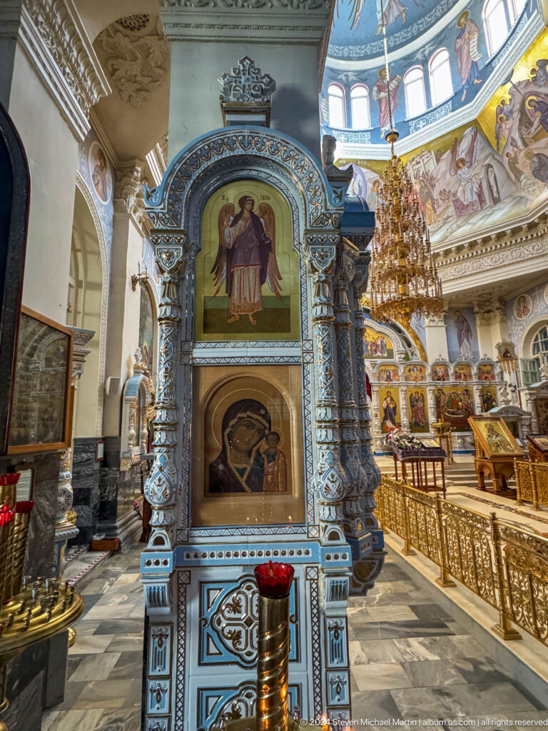 Tall ornate icon shrine with two religious images beside the cathedral iconostasis.