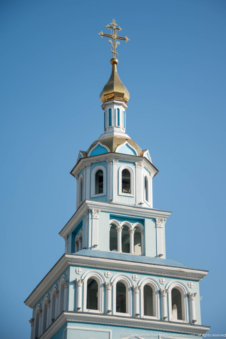 Close upward view of a pale blue bell tower with paired arches and a gilded dome.
