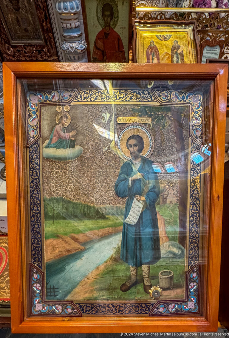 Framed Orthodox icon of a haloed young man in blue robes standing in a landscape.