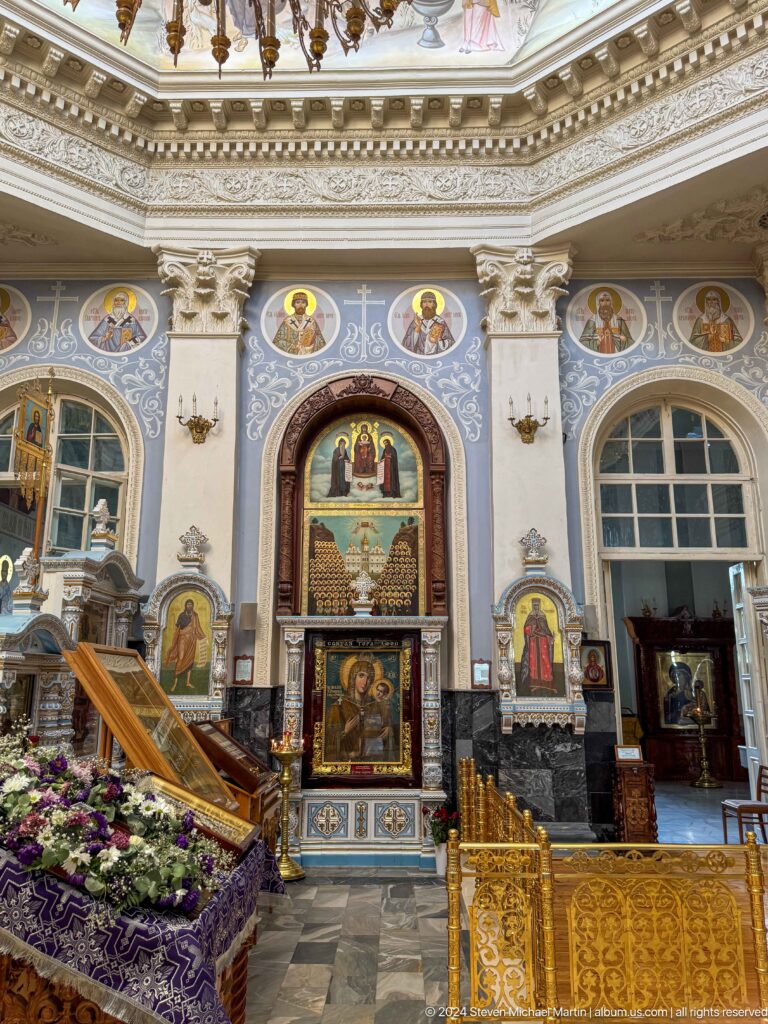Cathedral side shrine with a central icon, painted saints, white columns, and arched windows.