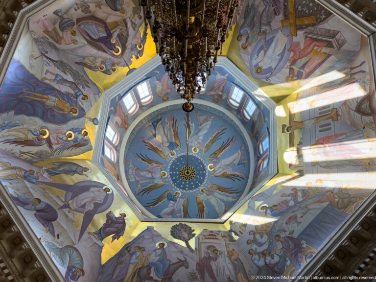 Upward view of a painted cathedral dome with angels surrounding a central blue medallion.