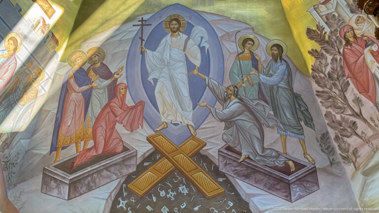 Mural of risen Christ with a cross above open tombs and gathered figures.