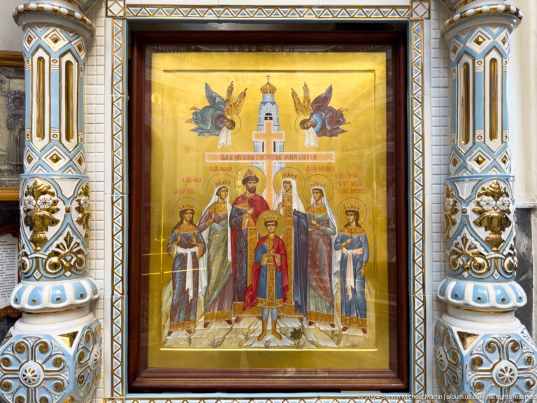 Gold icon of saints beneath a central cross and angels in an ornate frame.