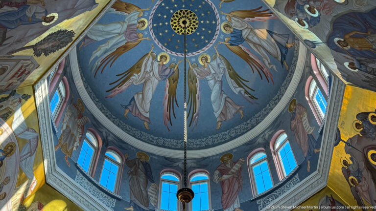 Blue cathedral dome with a star-filled center, angels, saints, and tall arched windows.