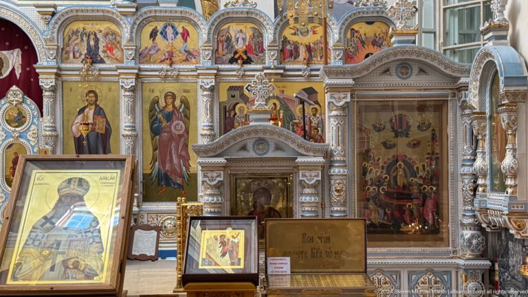 Cathedral side aisle densely filled with framed icons, painted saints, and devotional stands.
