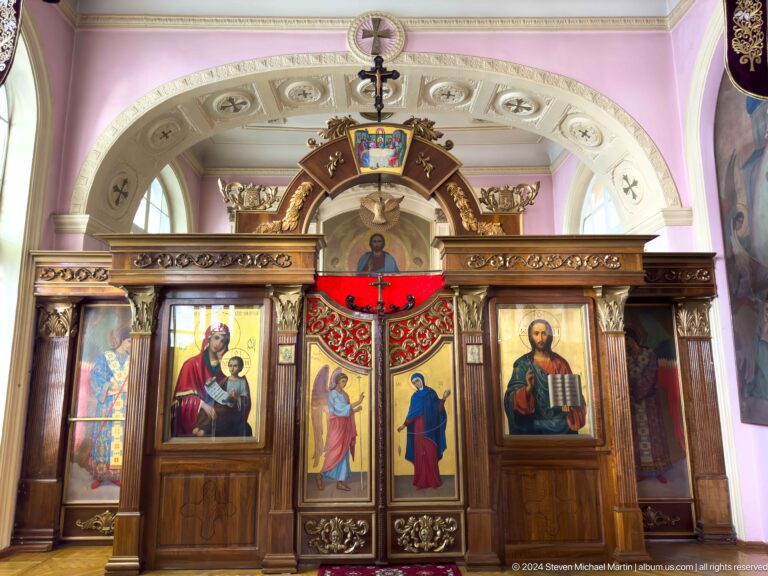 Dark wooden chapel screen with central doors, red canopy, and large icons of the Virgin and Christ.
