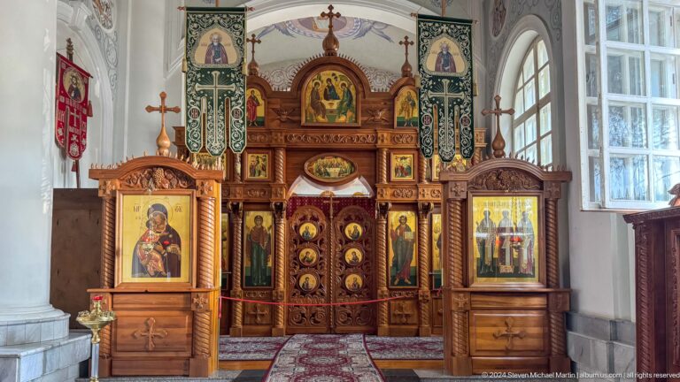 Frontal dark wooden chapel iconostasis with central doors and large icons on both sides.