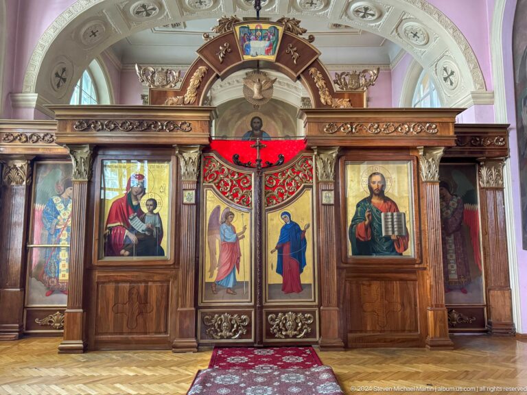 Close view of dark wooden iconostasis doors beneath a red canopy, flanked by large icons.