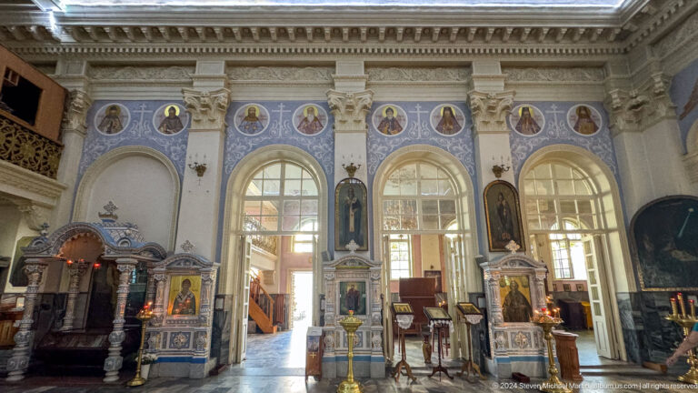 Cathedral side wall with tall arched windows, saint medallions, painted figures, and icon shrines.