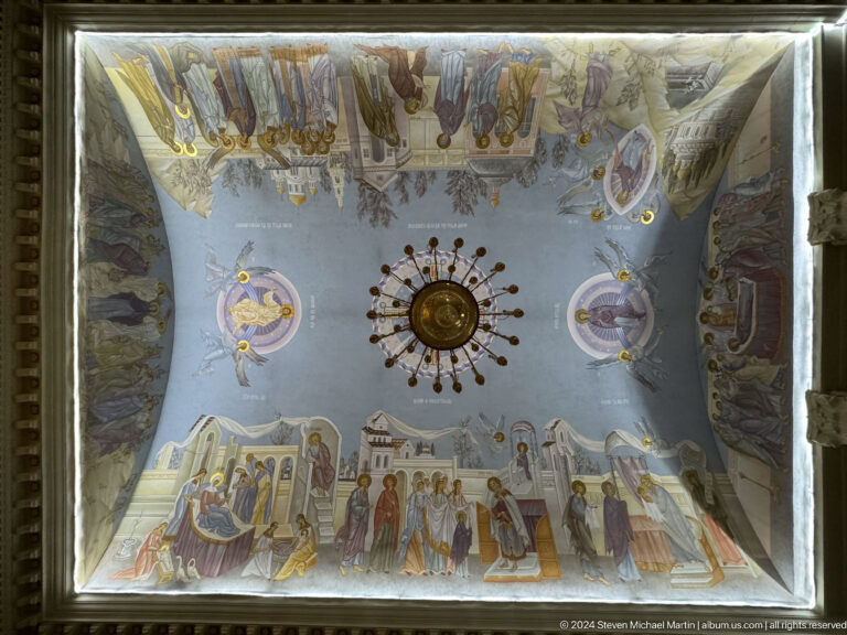Inverted reflection of a painted cathedral ceiling and central radiating metal fixture.