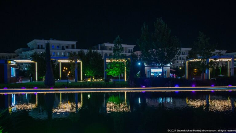 Night reflecting pool with repeated illuminated frames and low buildings mirrored across the water.