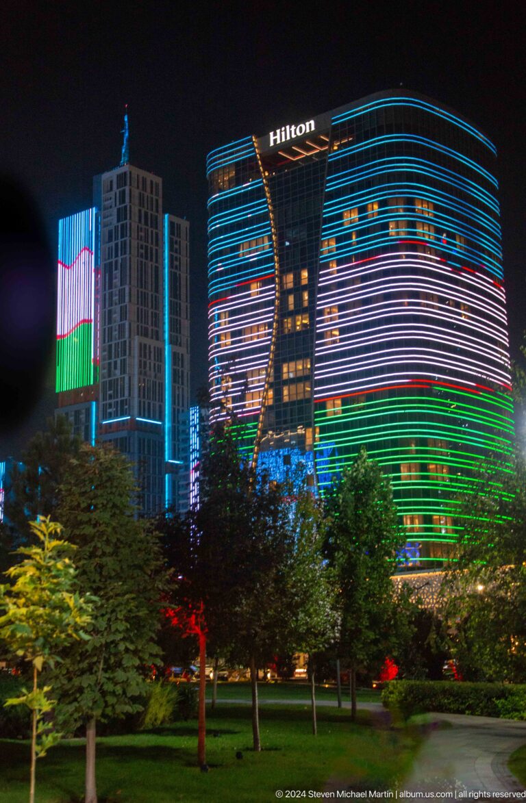 Close night view of curved glass towers wrapped in blue, white, red, and green horizontal lights.