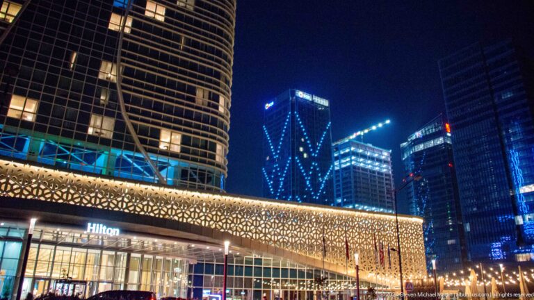 Night exterior of Hilton Tashkent City with a curved tower above a gold-lit geometric lattice facade.