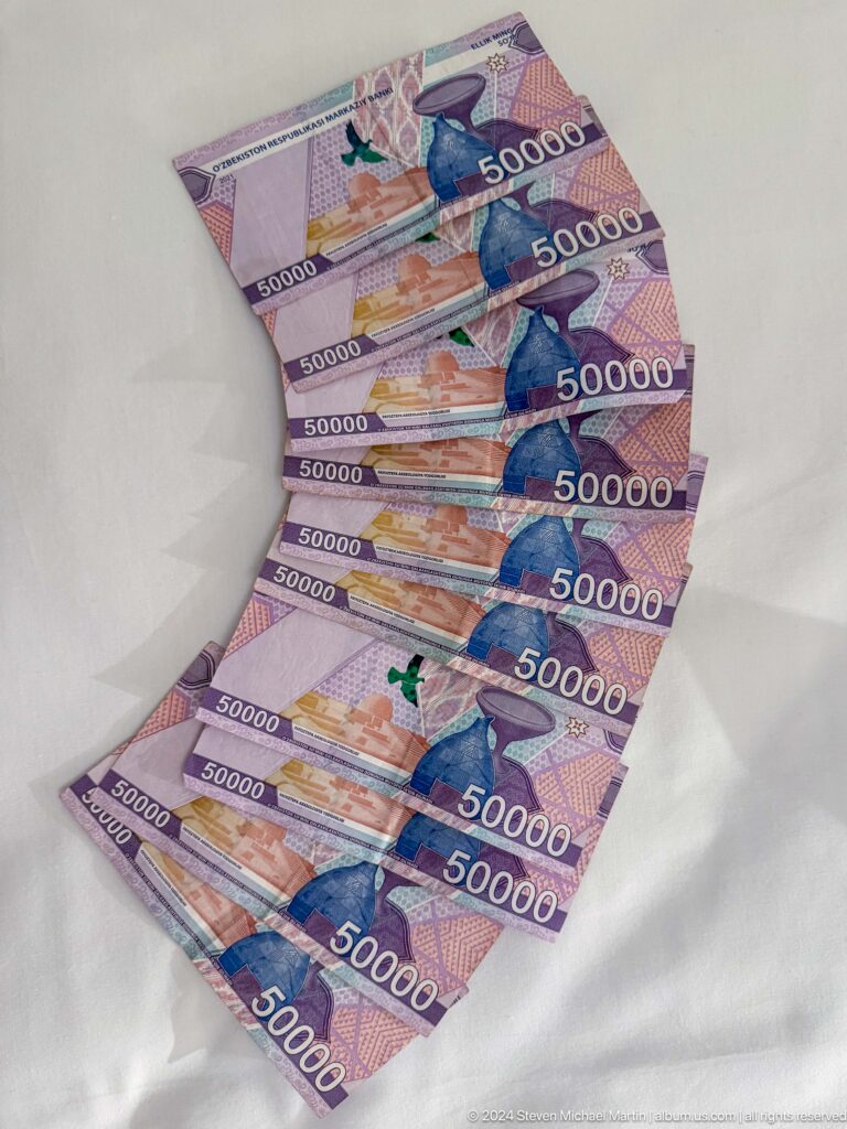 Several purple Uzbek 50,000-som banknotes arranged in a fan on a white surface.