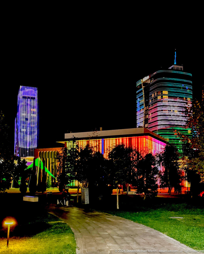 Red-lit low building between a purple tower and a multicolored curved high-rise at night.