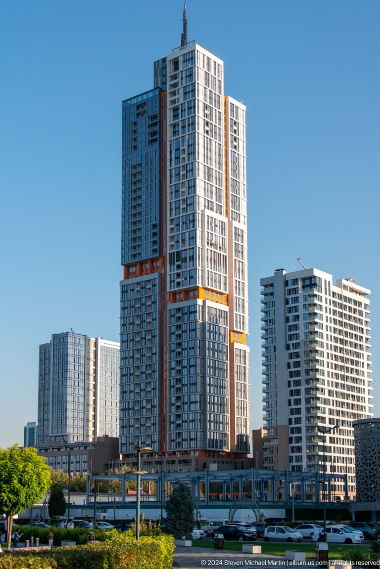 Three modern high-rise towers in daylight, including one with orange and yellow facade accents.