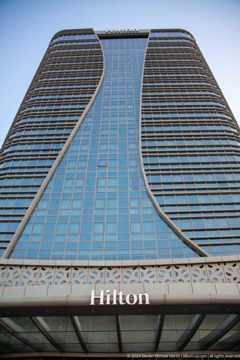 Close upward view of a curved blue-glass tower facade crossed by pale structural ribs.