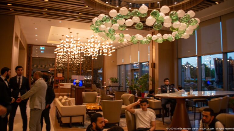 Hotel lounge with guests seated beneath clusters of green and white glass globe lights.
