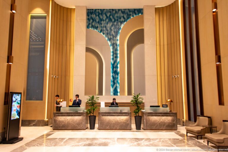 Symmetrical hotel reception with three desks, tall arches, gold-toned walls, and a blue patterned panel.