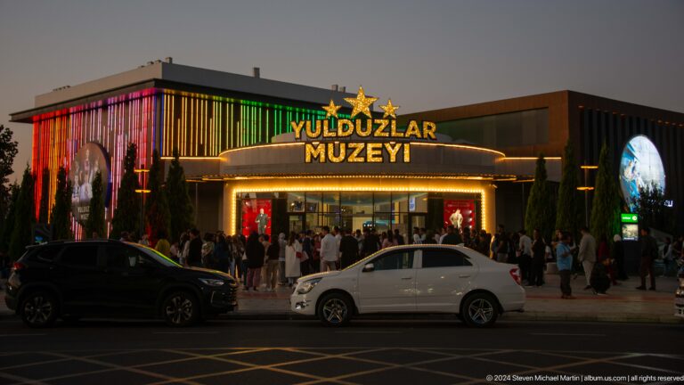 Evening crowd outside the brightly lit Yulduzlar Muzeyi entrance with star symbols and multicolored facade lights.