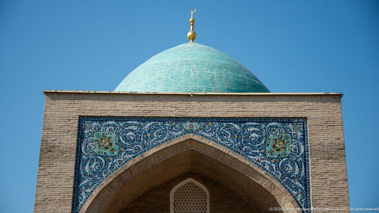 Pointed brick arch framed by blue floral tilework beneath turquoise dome at the Khast Imom complex in Tashkent.