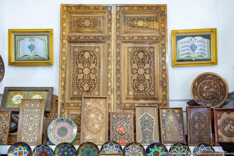Wooden carved panels, painted plates, framed art, and ornamental objects arranged indoors at the Khast Imom complex in Tashkent.