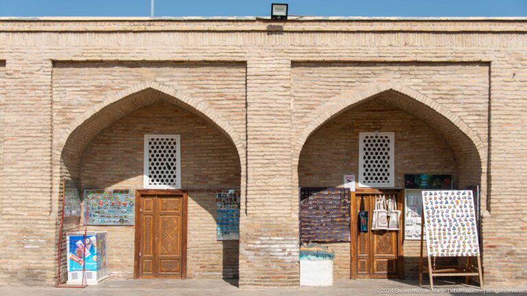 Two pointed brick bays with wooden doors, lattice windows, and displayed textiles at the Khast Imom complex in Tashkent.