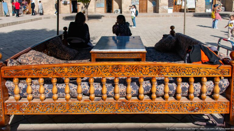 Embroidered fabrics draped across a balcony rail with seated figures behind at the Khast Imom complex in Tashkent.