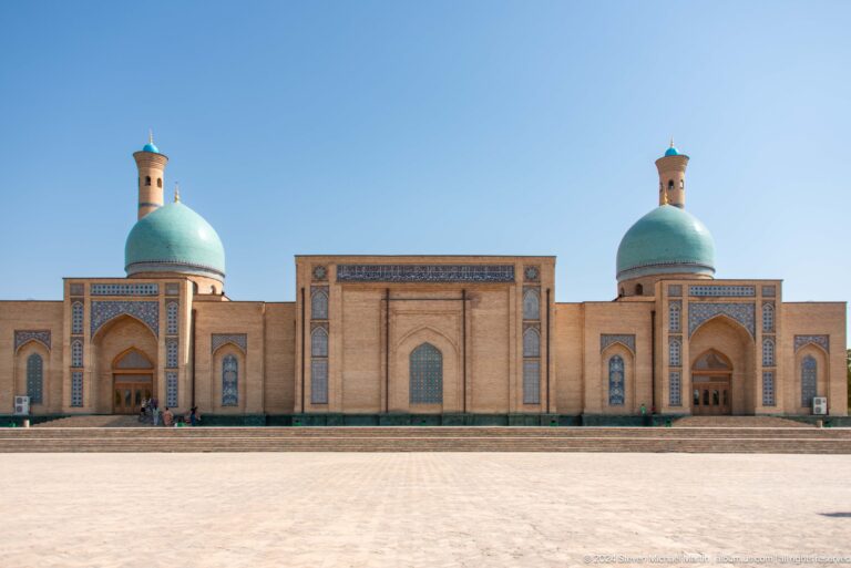 Long symmetrical brick elevation with turquoise domes across an empty paved square at the Khast Imom complex in Tashkent.