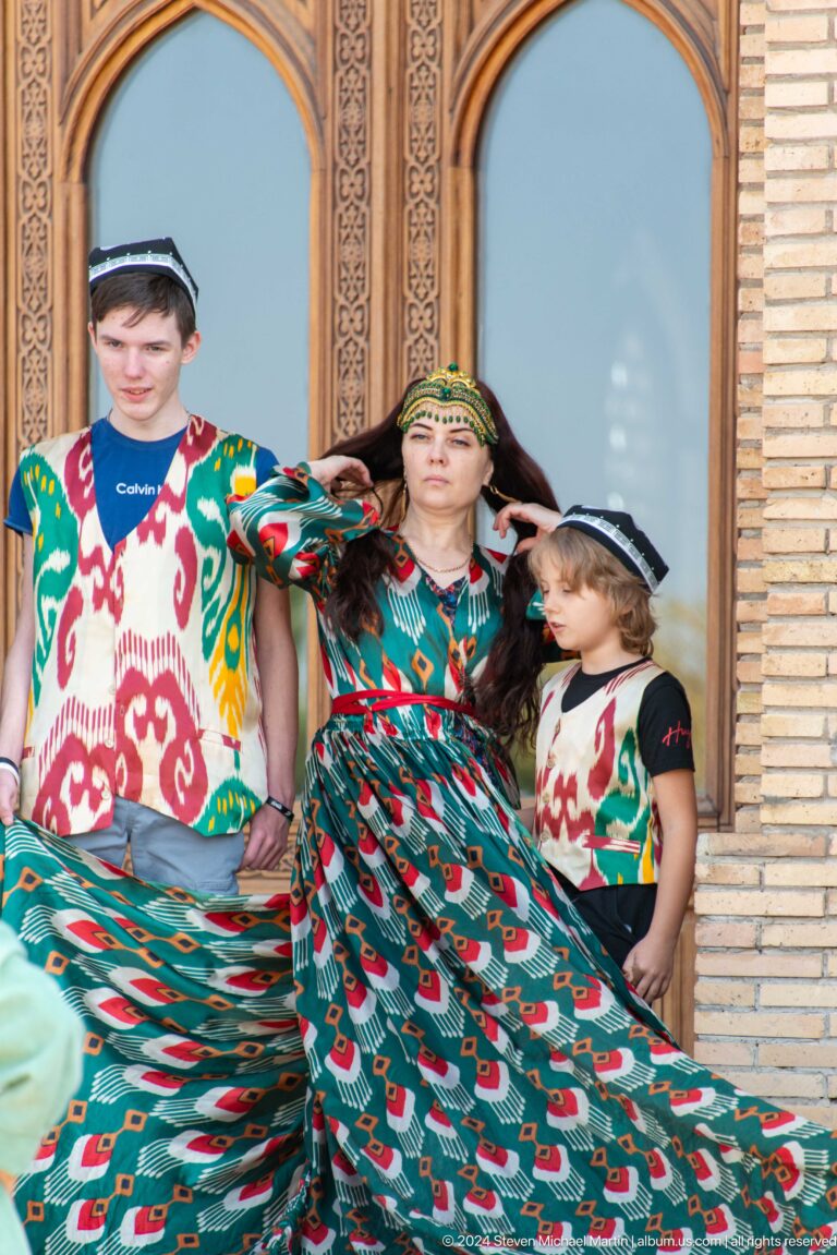 Adult and child posing beside brightly colored textiles at a craft stall at the Khast Imom complex in Tashkent.