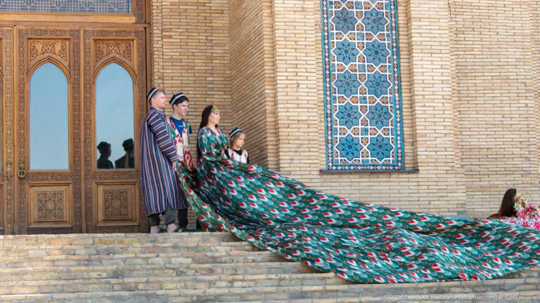 Group in traditional-style clothing holding an extended green-and-red fabric outside a brick building at the Khast Imom complex in Tashkent.