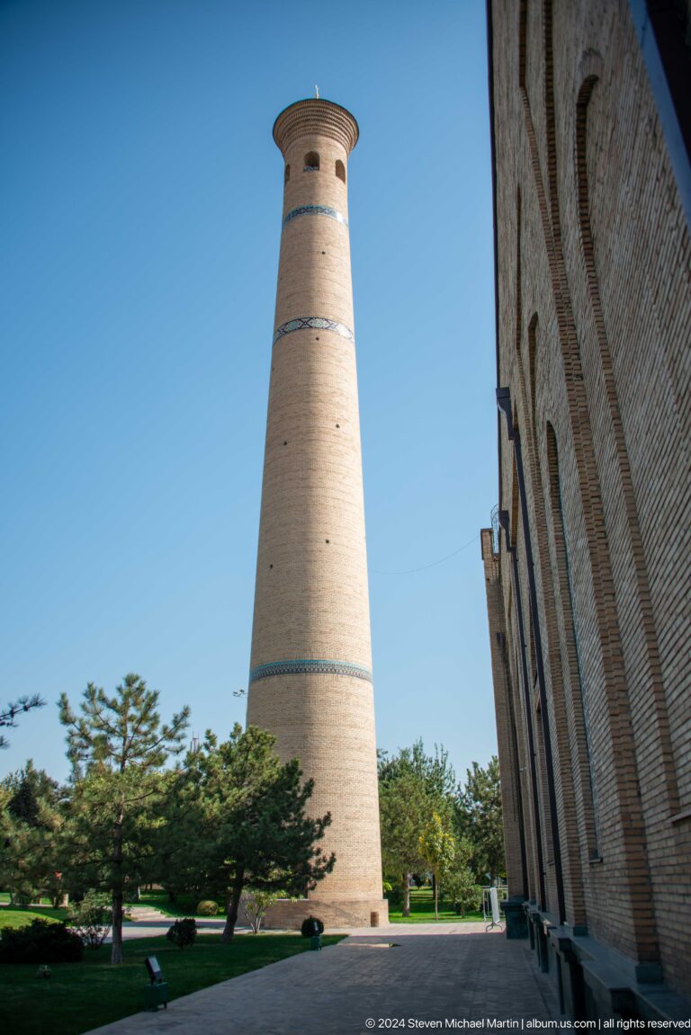 Slender pale-brick minaret rising in a narrow gap between masonry walls at the Khast Imom complex in Tashkent.