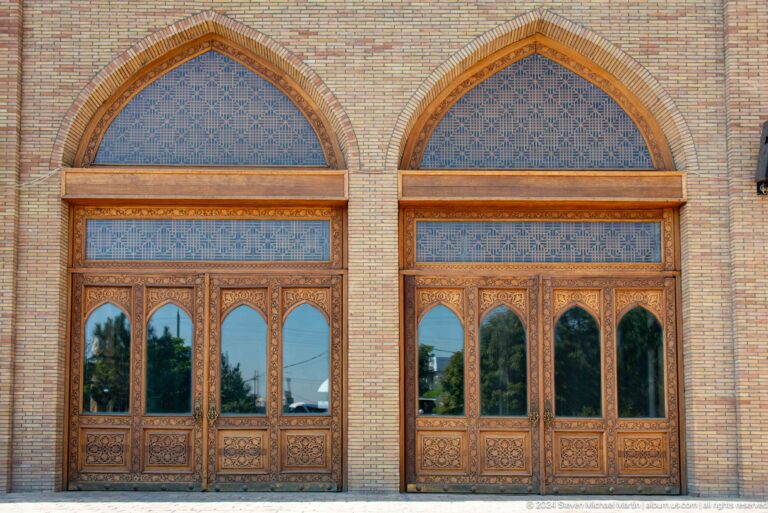 Paired arched bays with carved wooden doors and blue patterned tympana at the Khast Imom complex in Tashkent.
