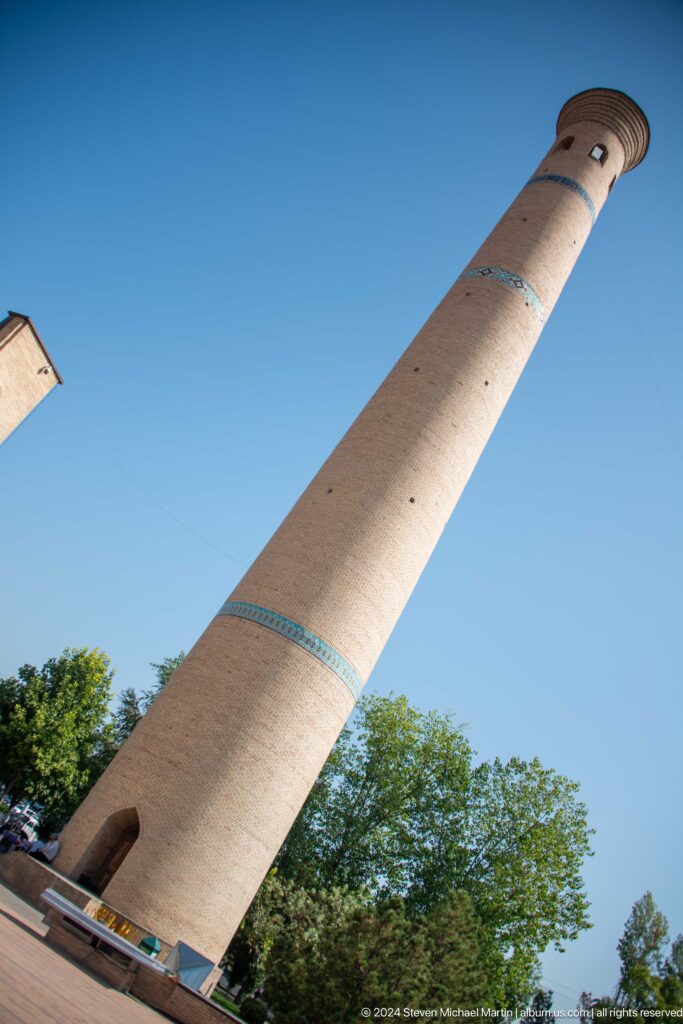 Diagonal cylindrical brick shaft crossed by a narrow turquoise tile band at the Khast Imom complex in Tashkent.
