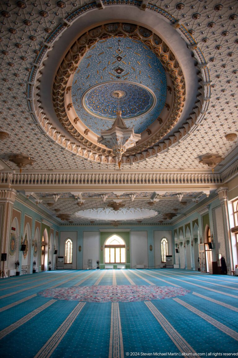 Wide interior view emphasizing carved cornice, painted dome, and central chandelier at the Khast Imom complex in Tashkent.
