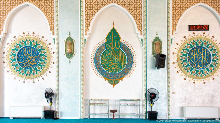 Three turquoise-and-gold arabic calligraphic medallions between arched wall bays at the Khast Imom complex in Tashkent.