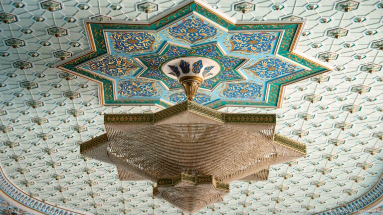 Large bronze-toned chandelier below a blue-green star-shaped coffer at the Khast Imom complex in Tashkent.