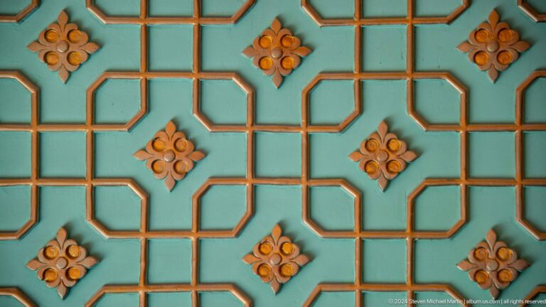 Turquoise grid of interlocking polygons punctuated by orange floral rosettes at the Khast Imom complex in Tashkent.