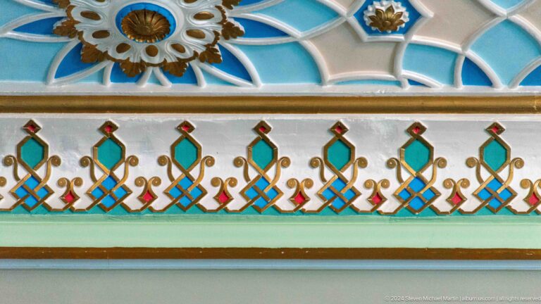 Repeating green, red, and gold floral forms along a white architectural band at the Khast Imom complex in Tashkent.