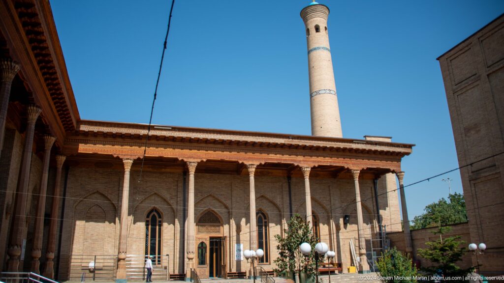 Timber-fronted religious building with brick minaret rising behind roofline at the Khast Imom complex in Tashkent.