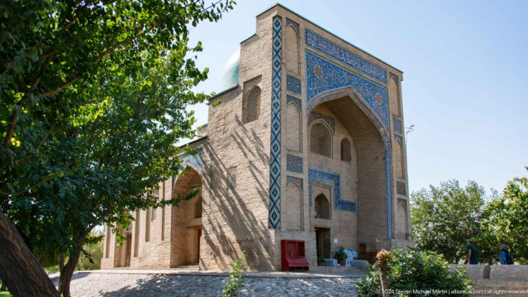 Compact brick structure with deep tiled portal, trees, and garden path at the Khast Imom complex in Tashkent.