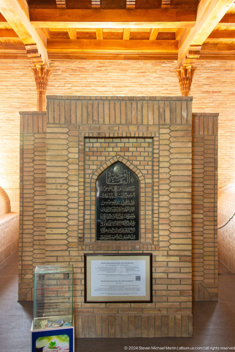 Dark arched plaque with several lines of light script set into tan brickwork at the Khast Imom complex in Tashkent.