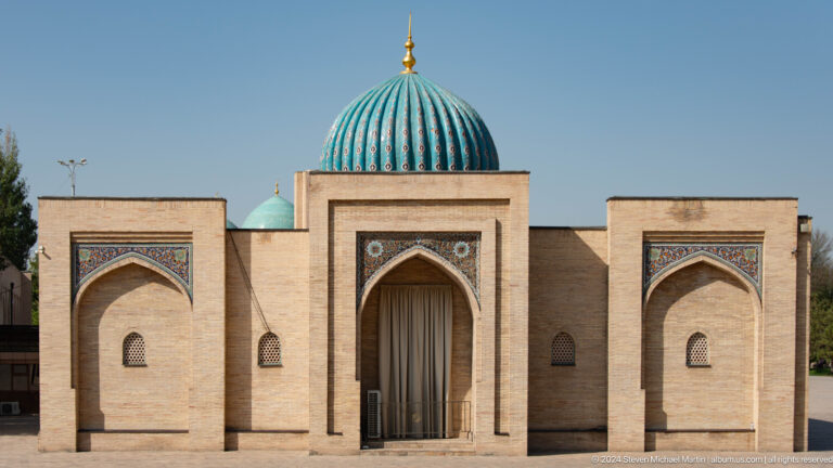 Symmetrical brick elevation with central pointed portal and turquoise ribbed dome at the Khast Imom complex in Tashkent.