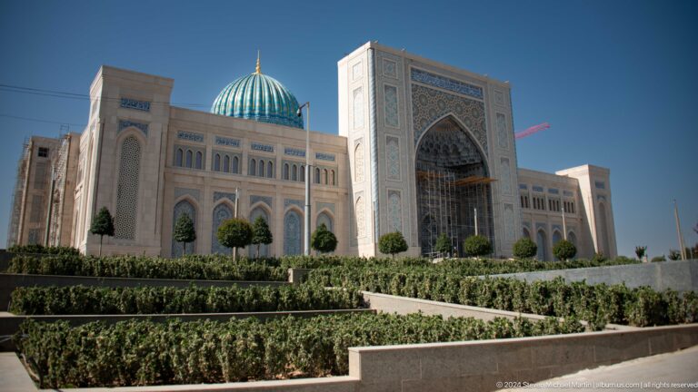 Angled view of pale monumental building, landscaped hedges, central portal, and blue dome at the Khast Imom complex in Tashkent.