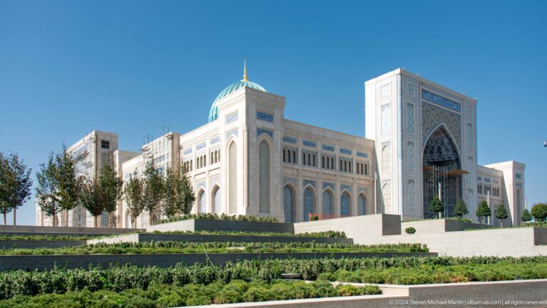 Long pale facade and tall portal tower seen beyond manicured gardens at the Khast Imom complex in Tashkent.