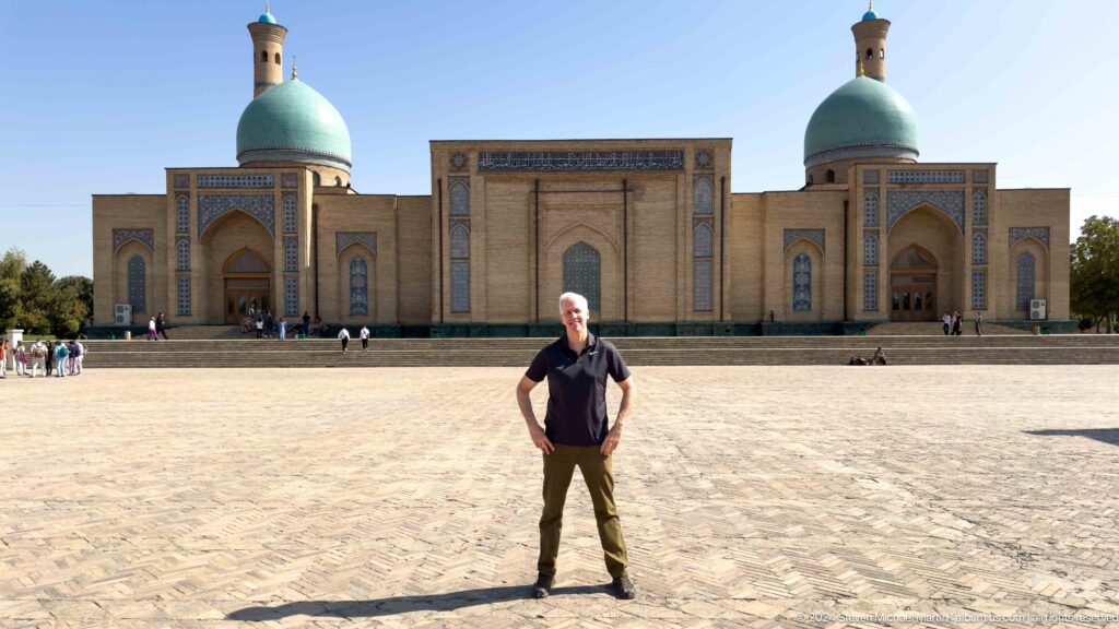 Man with backpack standing before symmetrical mosque facade and turquoise domes at the Khast Imom complex in Tashkent.