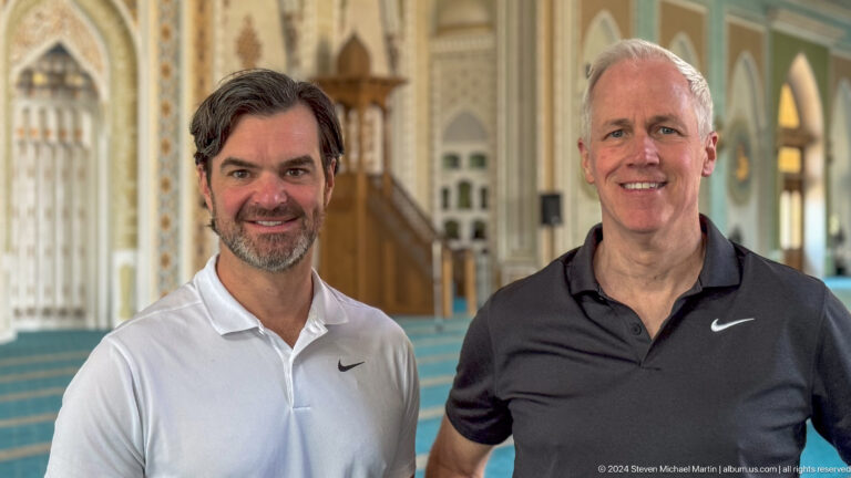 Two smiling men in polo shirts posed before an ornate prayer hall at the Khast Imom complex in Tashkent.