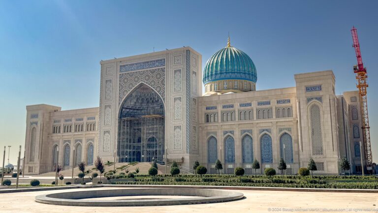 Broad frontal view of pale monumental building with central tiled arch and blue dome at the Khast Imom complex in Tashkent.