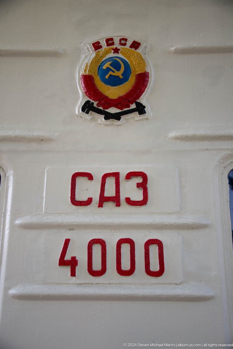 Red Cyrillic letters and partial numbers painted on a white ribbed railway equipment panel.